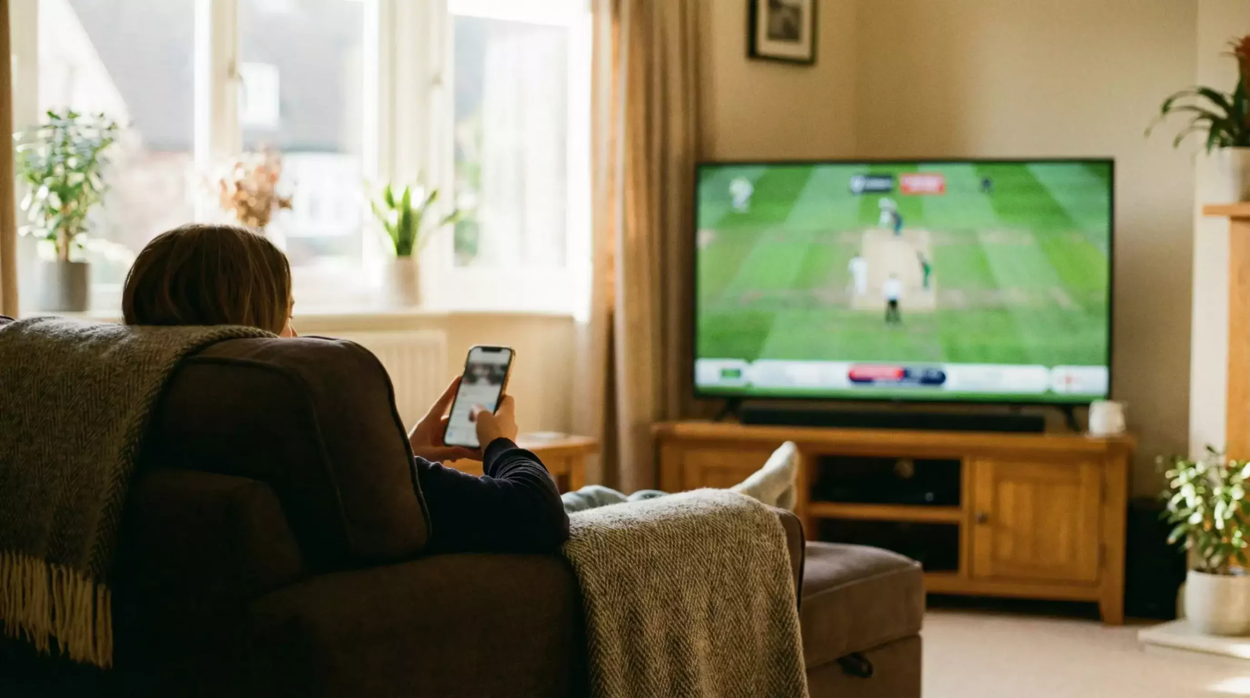 Person watching a cricket match on a mobile phone in a relaxed setting