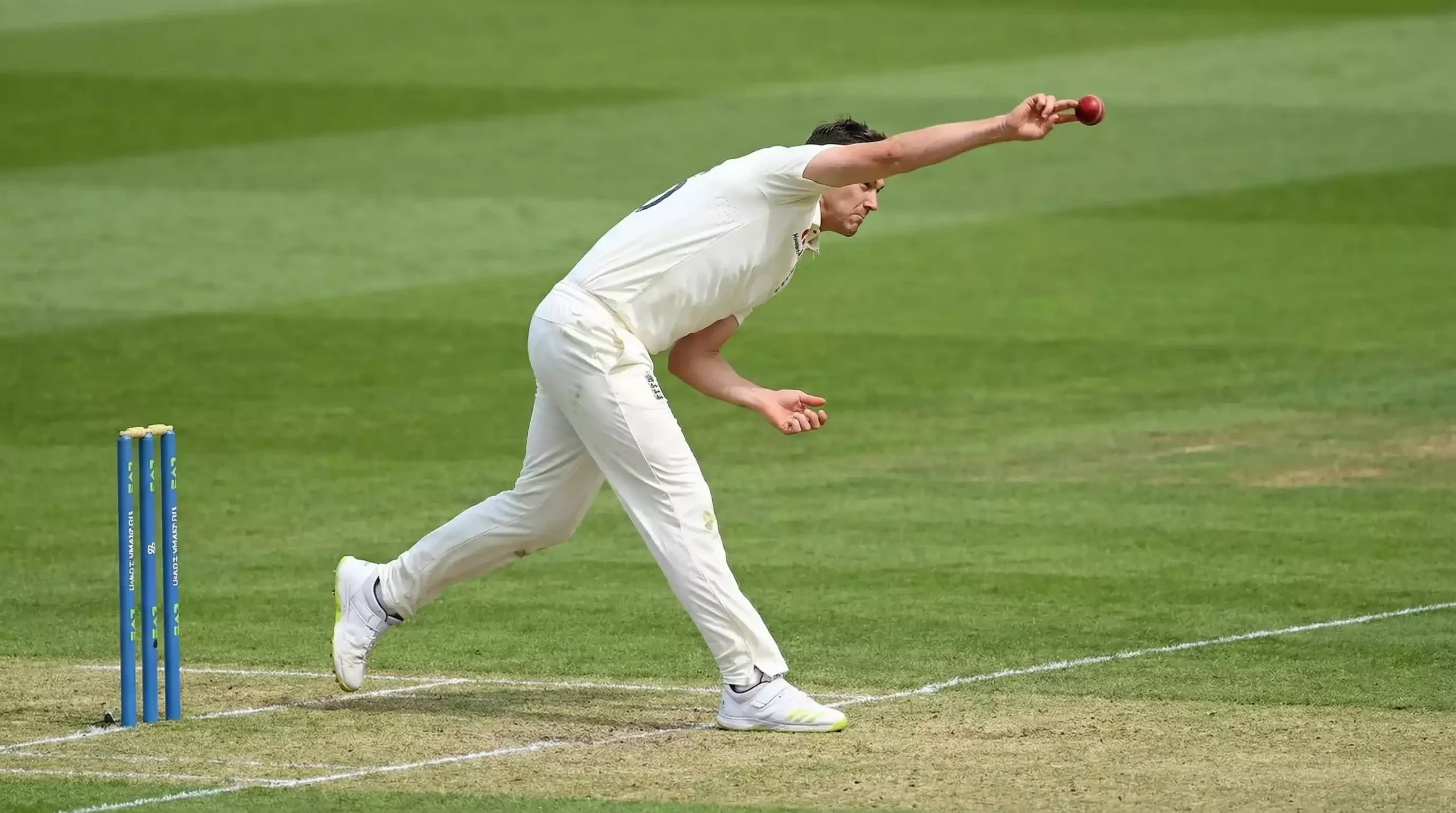 Fast bowler delivering a ball with stumps visible on a green cricket pitch